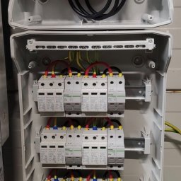 S.K.I. Master twoja złota rączka Kamil Dolata - Otwarta skrzynka elektryczna z bezpiecznikami i przewodami, widoczne narzędzia. Instalacja elektryczna wewnątrz obudowy, zabezpieczenia nadprądowe i różnicowoprądowe.