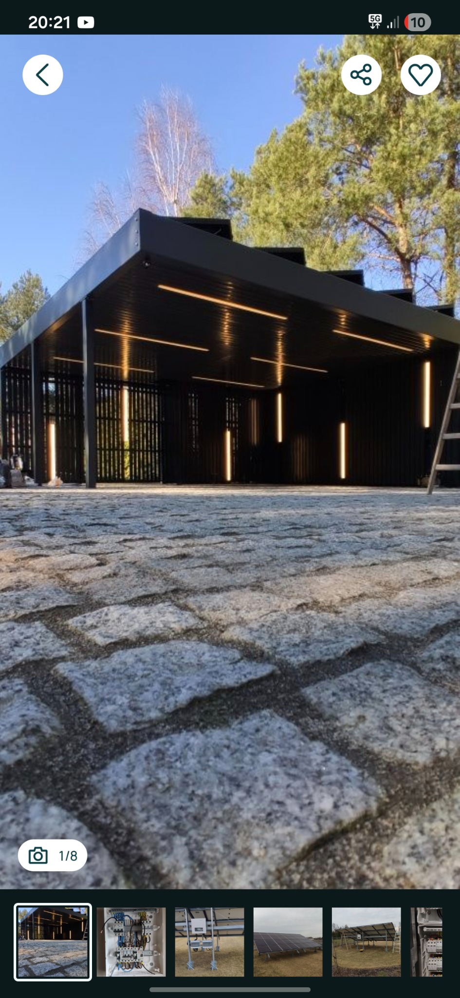 Nowoczesna, czarna altana z oświetleniem LED, widok z poziomu brukowanej nawierzchni. Minimalistyczny design, pionowe listwy, ciepłe światło.