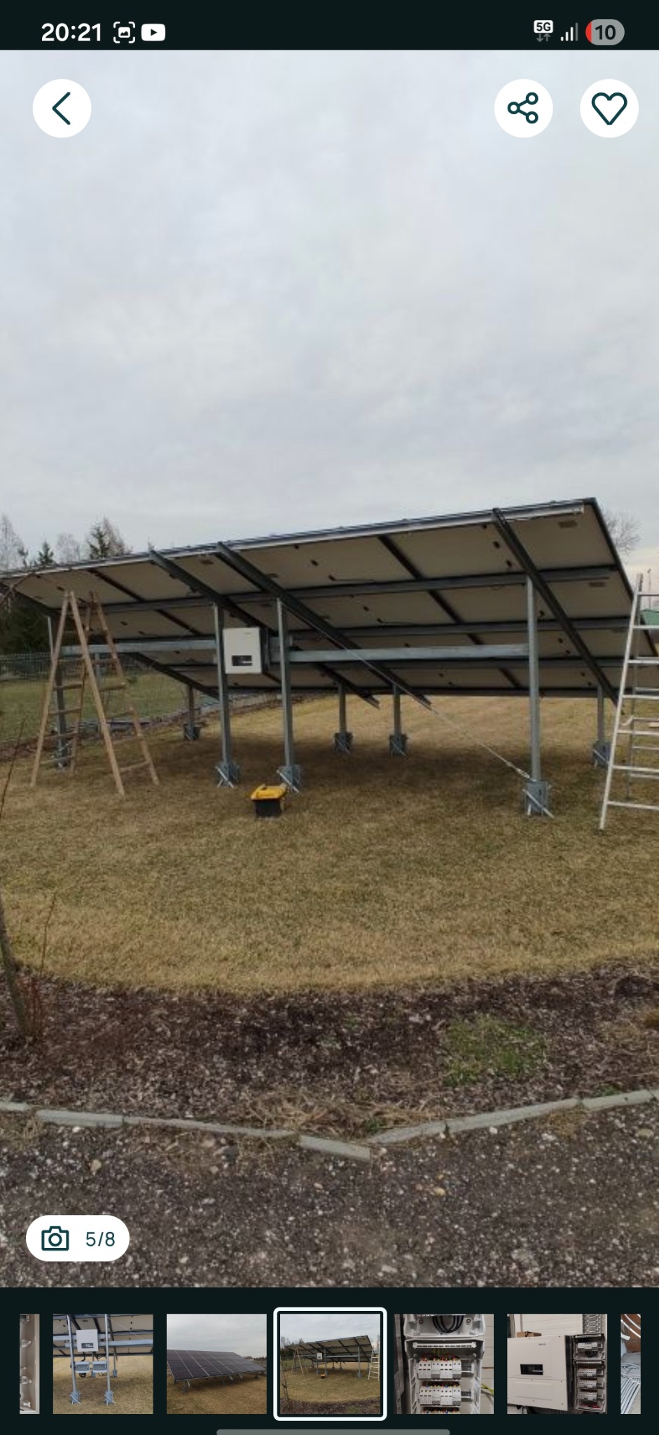 Montaż paneli fotowoltaicznych na konstrukcji wsporczej, widok z dołu, drabiny i skrzynka narzędziowa obok. Instalacja w trakcie realizacji na trawiastym terenie.