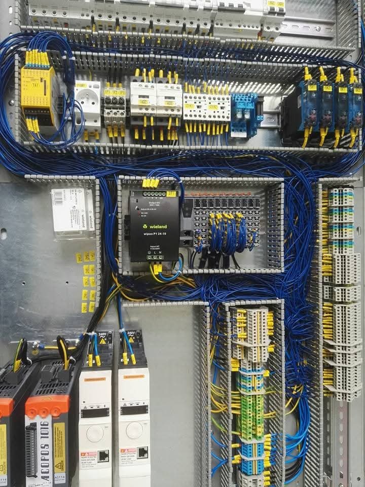 Rozbudowana szafa sterownicza z precyzyjnie ułożonymi przewodami, modułami i elementami automatyki, tworząca złożony system elektryczny w metalowej obudowie.