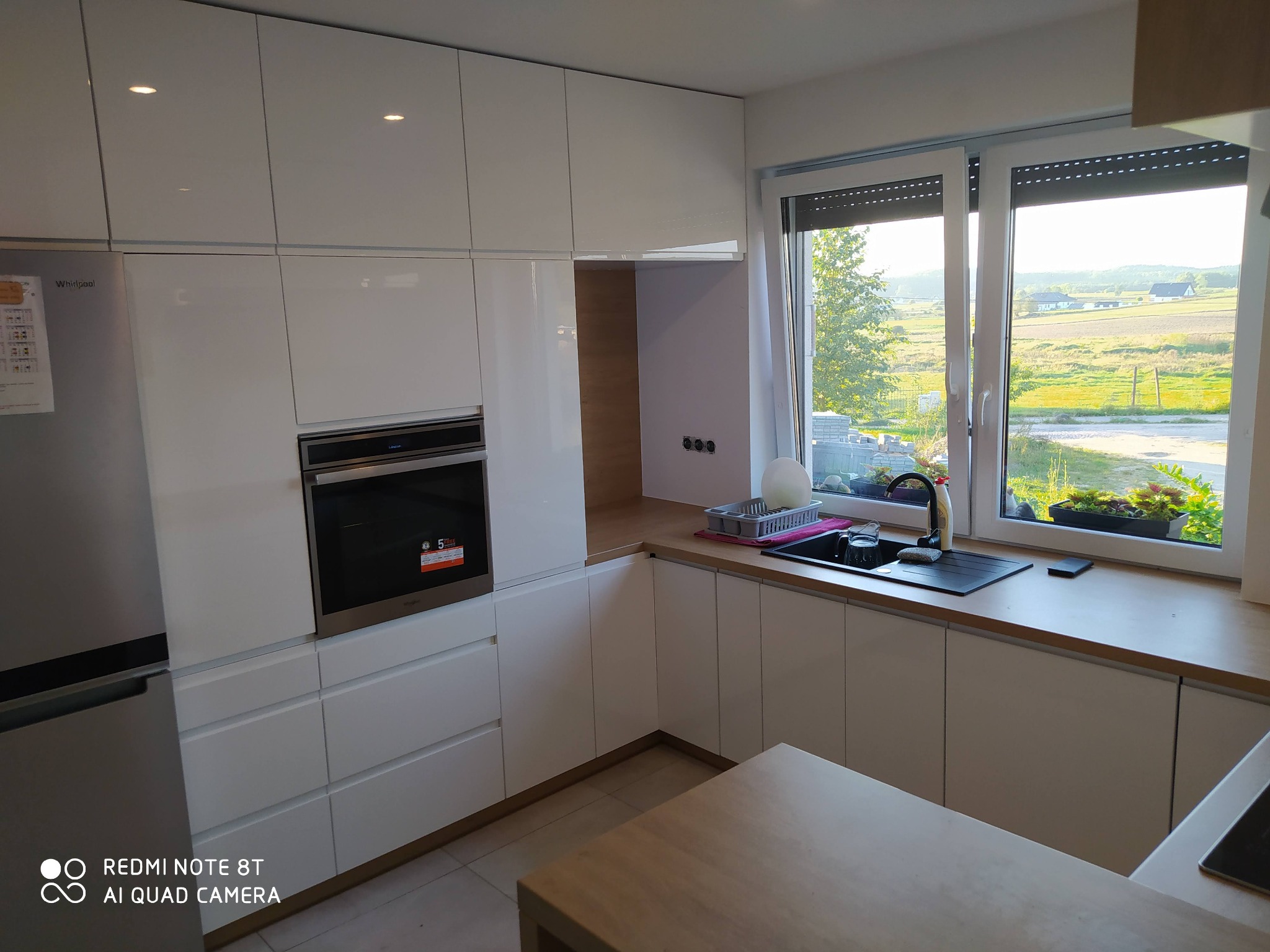 Biała, lakierowana kuchnia na wymiar z wbudowanym piekarnikiem Whirlpool i widokiem na wiejski krajobraz za oknem.
