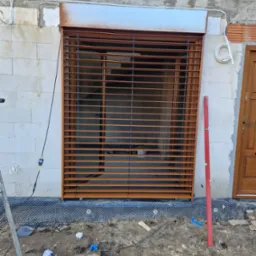 Montaż zewnętrznej rolety w kolorze brązowym na surowej ścianie z betonu komórkowego, widoczny poziomica, narzędzia i przewody na ziemi.