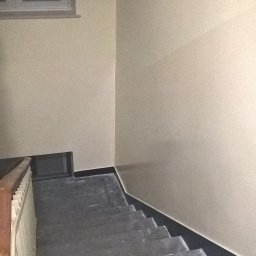 BAD-BUD - Klatka schodowa z szarymi, kamiennymi schodami i świeżo pomalowanymi na beżowo ścianami, widok z góry.