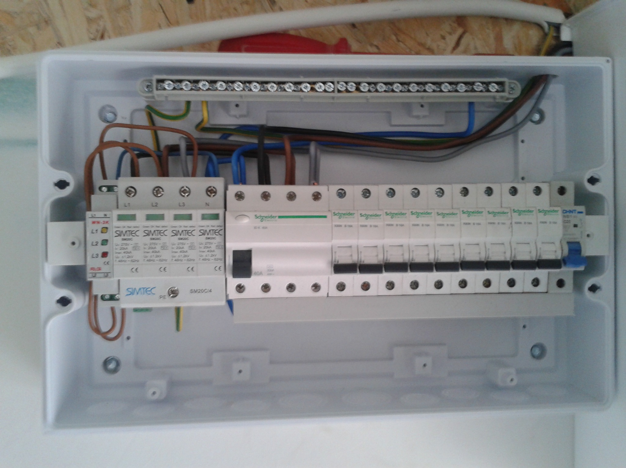 Otwarta skrzynka elektryczna z zainstalowanymi bezpiecznikami, przewodami i modułami Simtec, widoczne śruby mocujące i oznaczenia na urządzeniach.