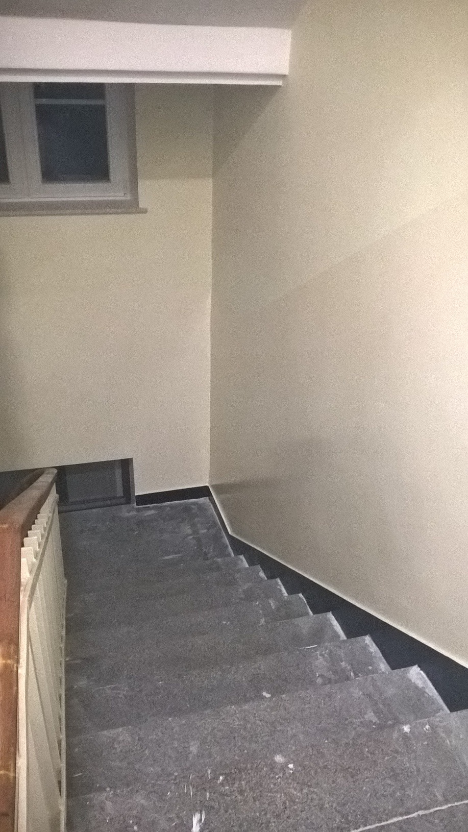 Klatka schodowa z szarymi, kamiennymi schodami i świeżo pomalowanymi na beżowo ścianami, widok z góry.