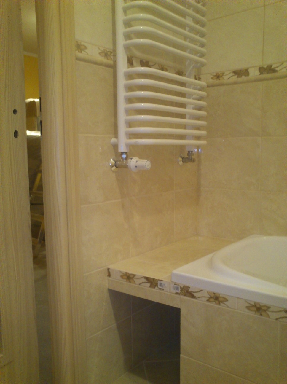 Beżowa łazienka z grzejnikiem drabinkowym, płytkami z motywem kwiatowym i fragmentem wanny.