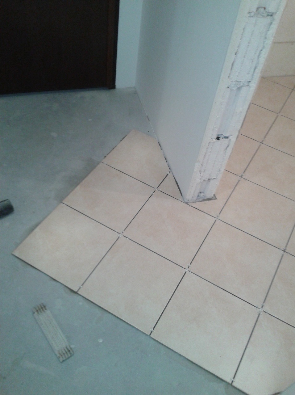 Układanie beżowych płytek podłogowych w trakcie remontu w Konstancin-Jeziorna, widoczne krzyżyki dystansowe i surowa ściana.