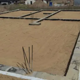 Przygotowanie fundamentów pod budowę domu, z widocznymi zbrojeniami i izolacją, teren wyrównany piaskiem.