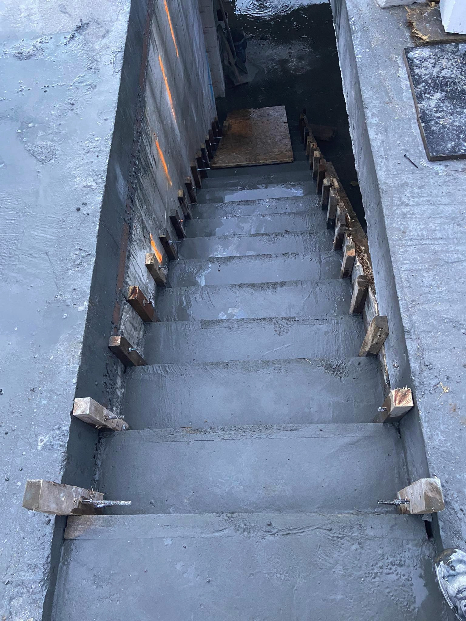 Surowe, betonowe schody w trakcie budowy, z drewnianymi elementami szalunku i wystającymi prętami zbrojeniowymi.