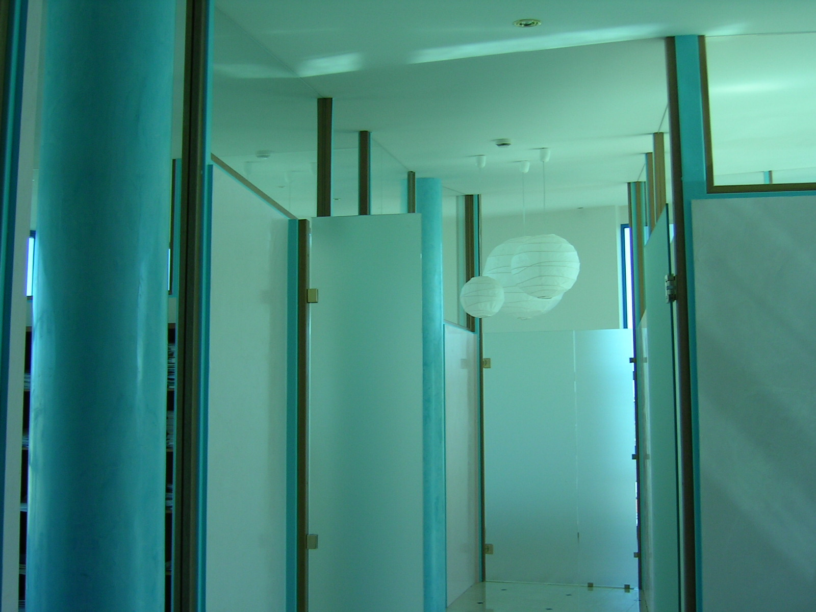 Nowoczesna łazienka z kabinami prysznicowymi oddzielonymi szklanymi ściankami, turkusowe kolumny i wiszące lampy kuliste.