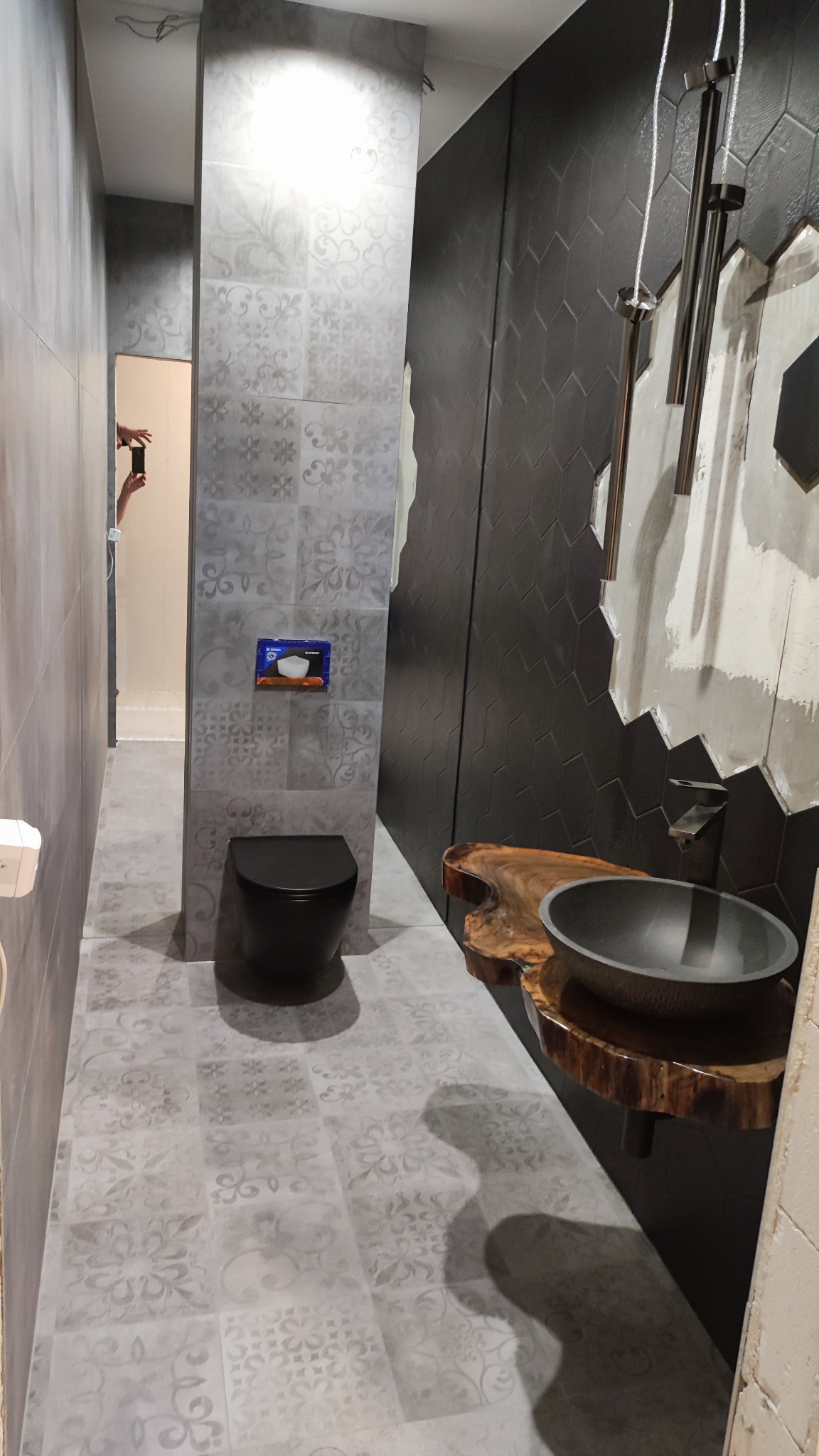 Nowoczesna łazienka z czarną miską WC, umywalką na drewnianym blacie i szarą mozaiką na ścianach.