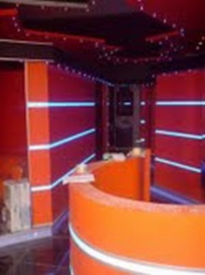 Narożnik pokoju z pomarańczową, półokrągłą ścianką działową, czerwonymi ścianami z białymi paskami i oświetleniem LED na suficie, w trakcie prac wykończeniowych.