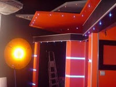 Pomarańczowo-czarne wykończenie wnętrza z dekoracyjnym oświetleniem sufitowym i kolumnami, widoczna drabina w tle.