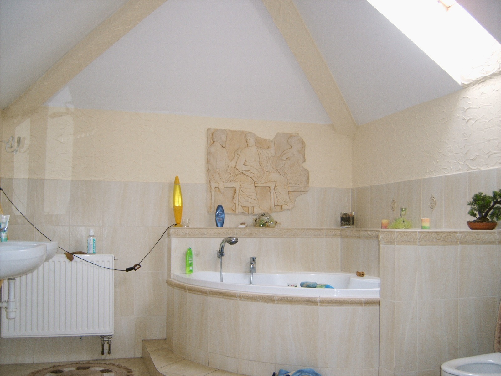 Jasna łazienka na poddaszu z wanną narożną, grzejnikiem żeberkowym i płaskorzeźbą nad wanną