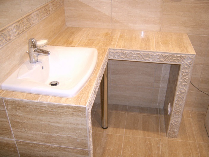 Beżowa łazienka z umywalką i blatem wykończonym dekoracyjną listwą, chromowany kran i mydelniczka.