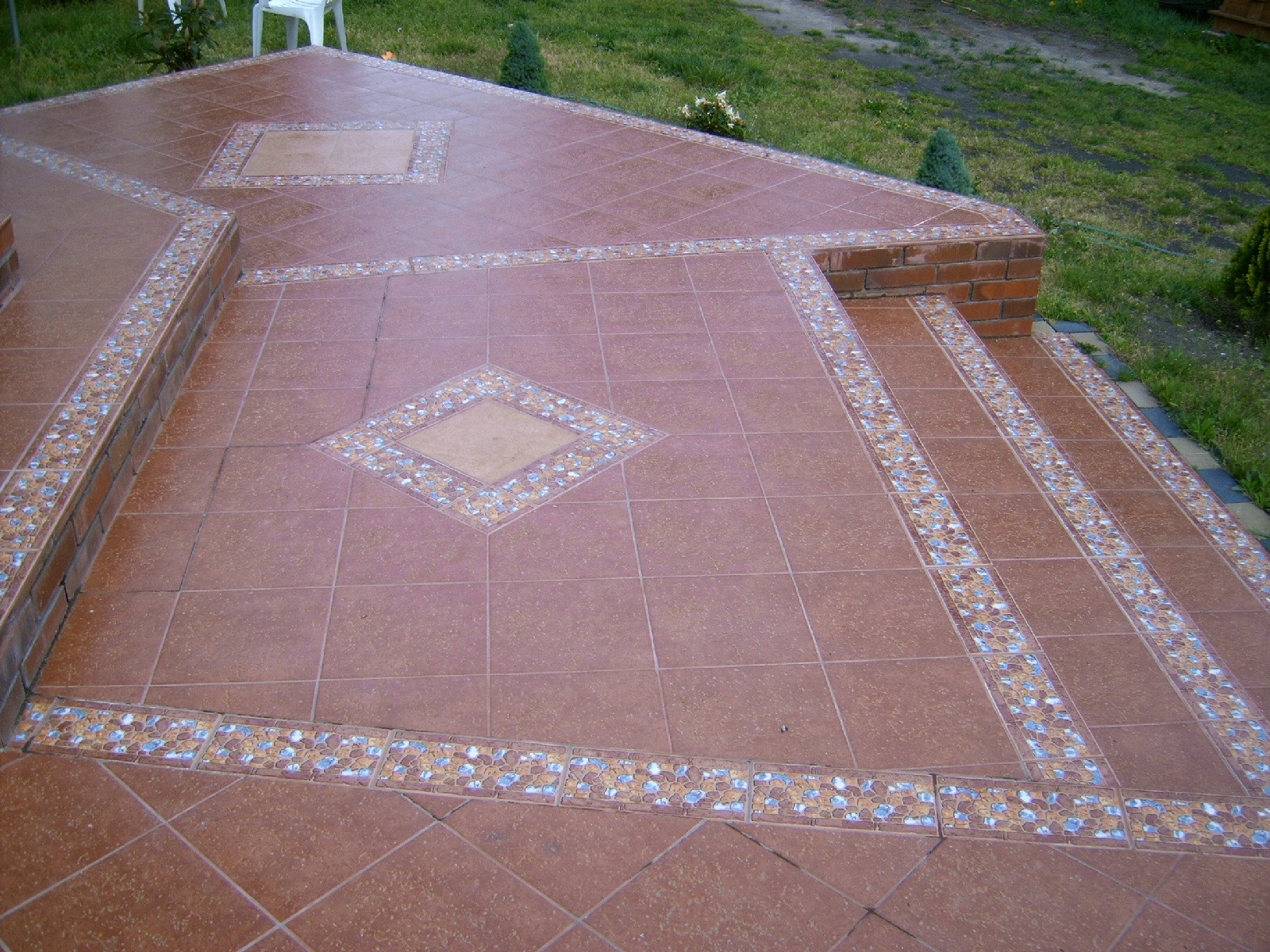 Wykończony taras z brązowych płytek z dekoracyjnymi obramowaniami i schodami wyłożonymi płytkami, widok z góry.