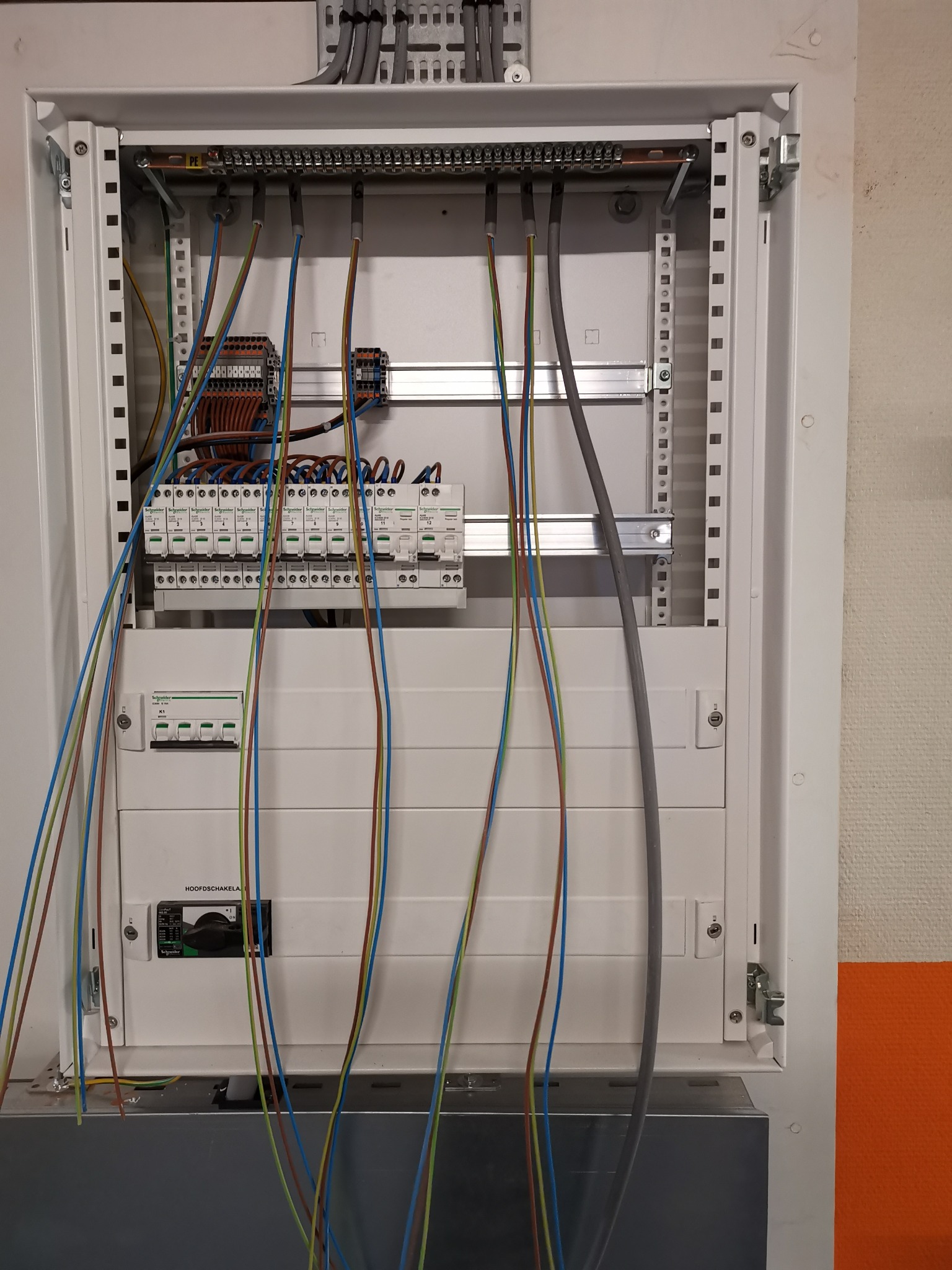 Otwarta, biała skrzynka elektryczna z zainstalowanymi bezpiecznikami i przewodami o różnych kolorach, widoczna część instalacji elektrycznej.