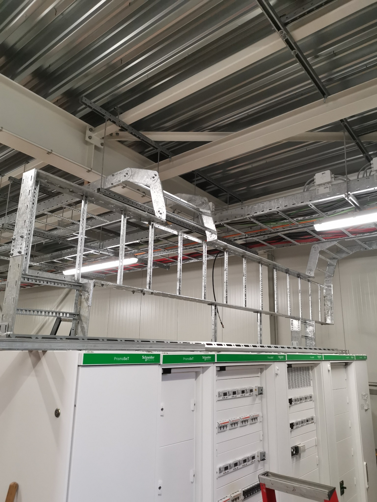 Rozdzielnica elektryczna PrismaSeT Schneider Electric z zamontowanymi zabezpieczeniami, widoczne koryta kablowe pod sufitem z ułożonymi przewodami.
