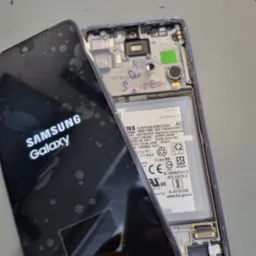 Rozłożony telefon Samsung Galaxy A52 z widocznym ekranem z logo i wnętrzem obudowy, przygotowany do wymiany ekranu, widoczne ślady po kleju na wyświetlaczu.