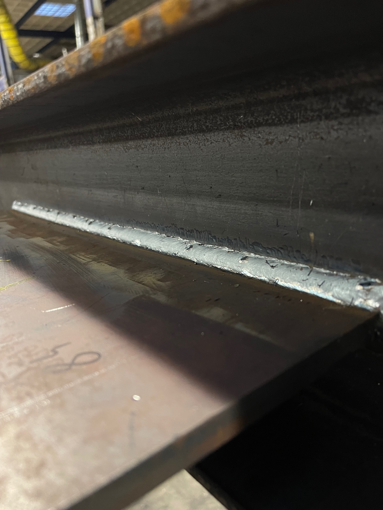 Spoina łącząca dwie metalowe płyty, widoczne drobne nierówności i przypalenia wzdłuż linii złączenia, surowy industrialny detal.