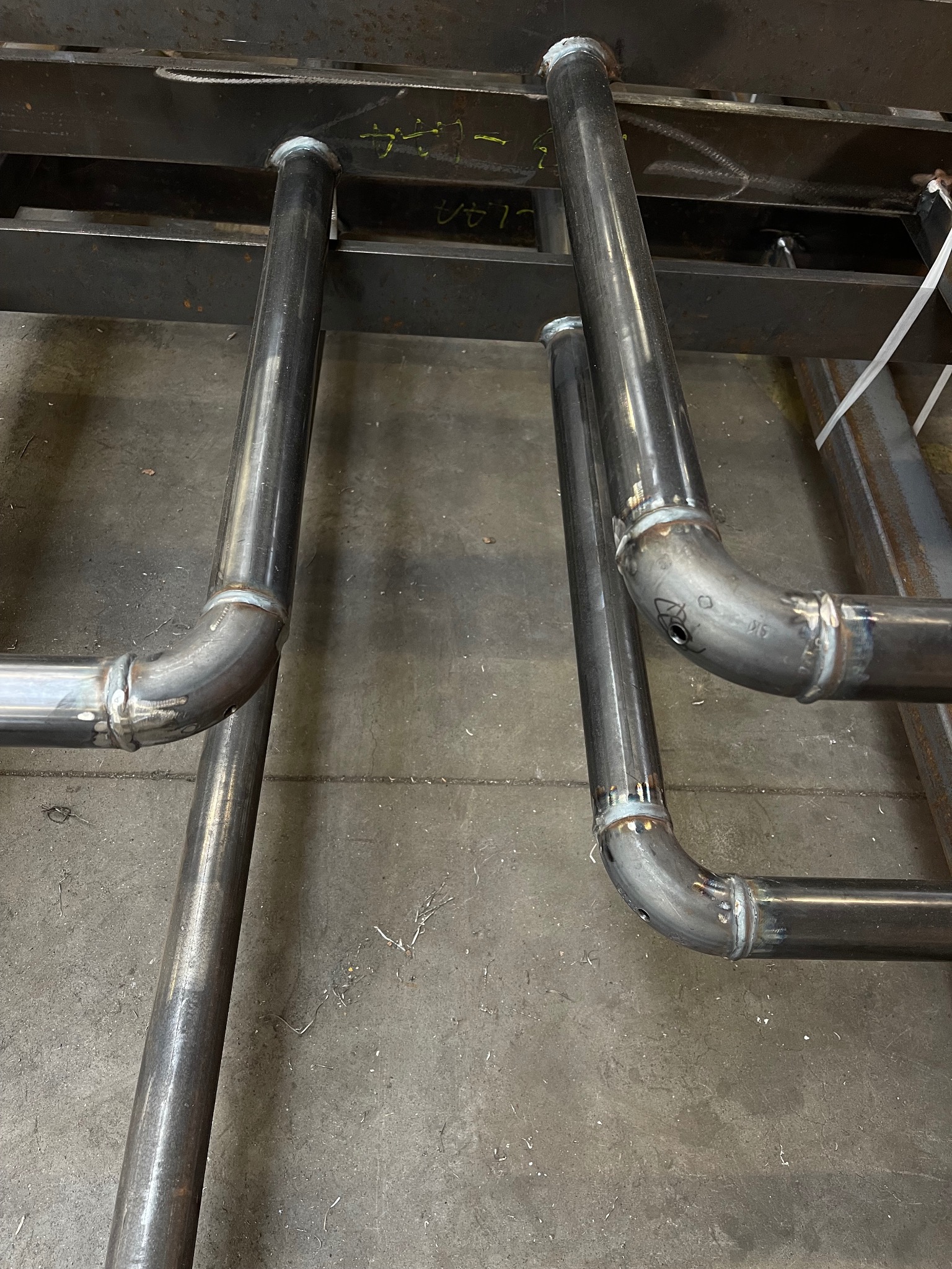 Surowe, metalowe rury połączone spawami, tworzące konstrukcję. Widoczne ślady obróbki i niedoskonałości spoin.