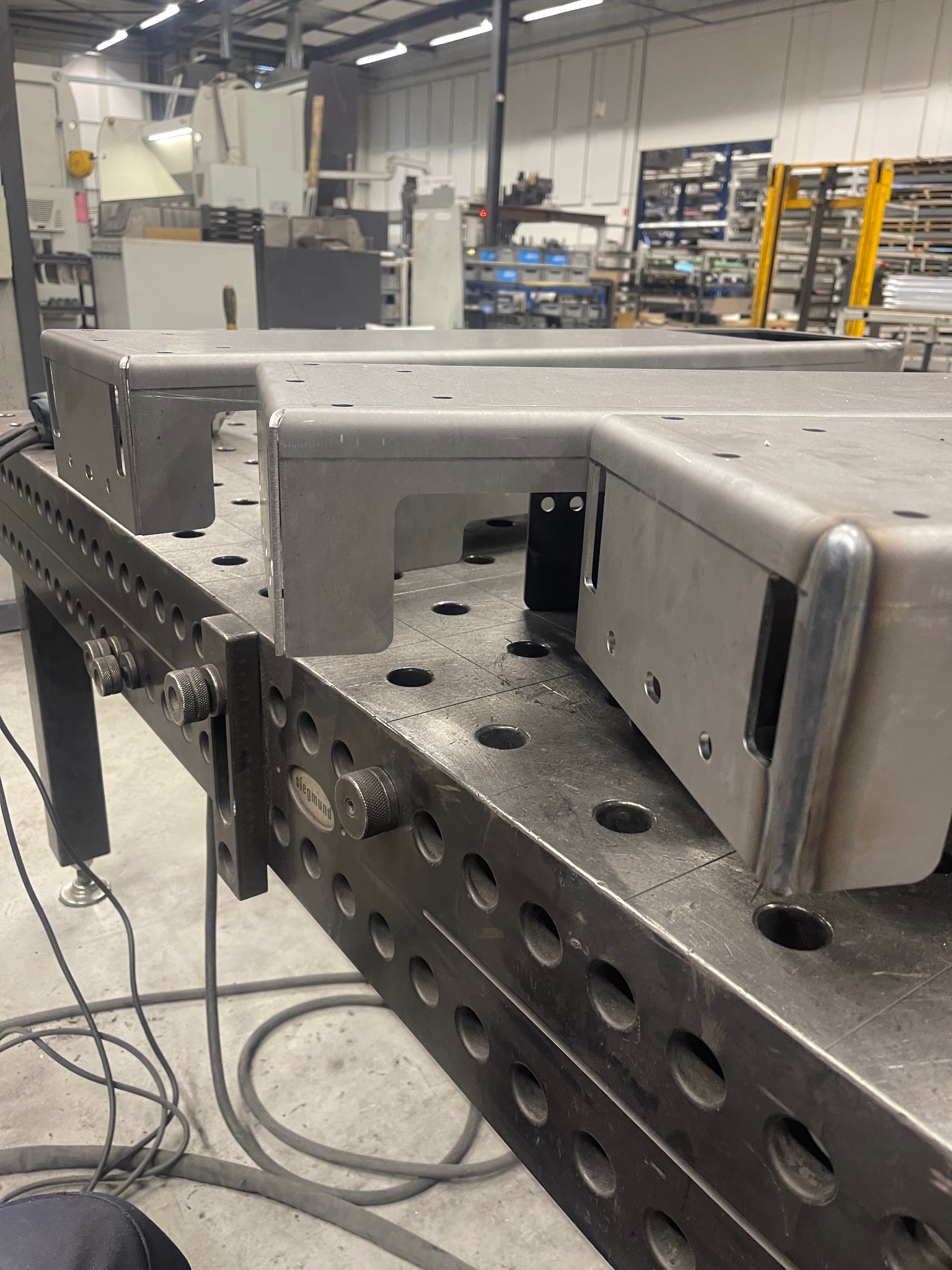 Metalowe elementy konstrukcyjne, spawane, ustawione na perforowanym stole spawalniczym Siegmund w hali produkcyjnej.
