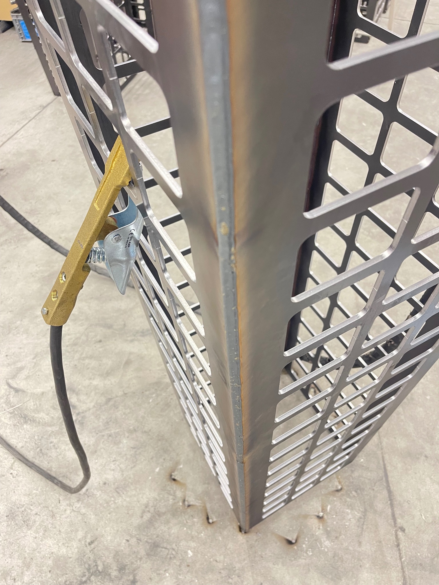 Metalowa konstrukcja kratowa, z widocznym uchwytem spawalniczym, prawdopodobnie w trakcie łączenia elementów.