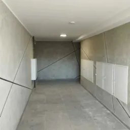 Korytarz w budynku z szarymi płytkami podłogowymi i dekoracyjnymi ścianami z geometrycznym wzorem. Białe szafki na ścianie po prawej stronie.