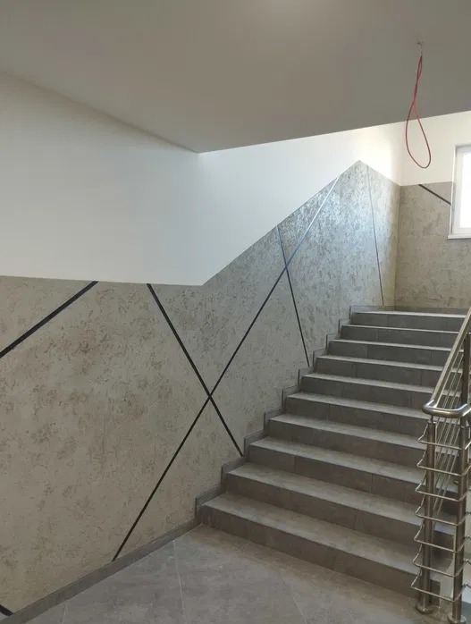 Klatka schodowa po remoncie w Koszalinie: ściany z dekoracyjną fakturą i geometrycznym wzorem, schody wyłożone płytkami, metalowa balustrada.