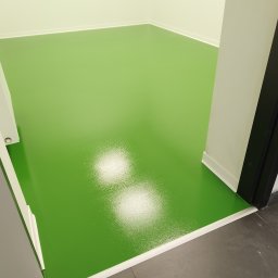 Michał Dobija - Błyszcząca, jasnozielona posadzka żywiczna w pomieszczeniu w Łodygowicach, widoczna z perspektywy wejścia, z białymi listwami przypodłogowymi i framugą drzwi.