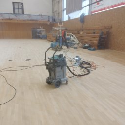 Michał Dobija - Cyklinowanie parkietu w hali sportowej, widoczny sprzęt Bona i pracownik w tle.