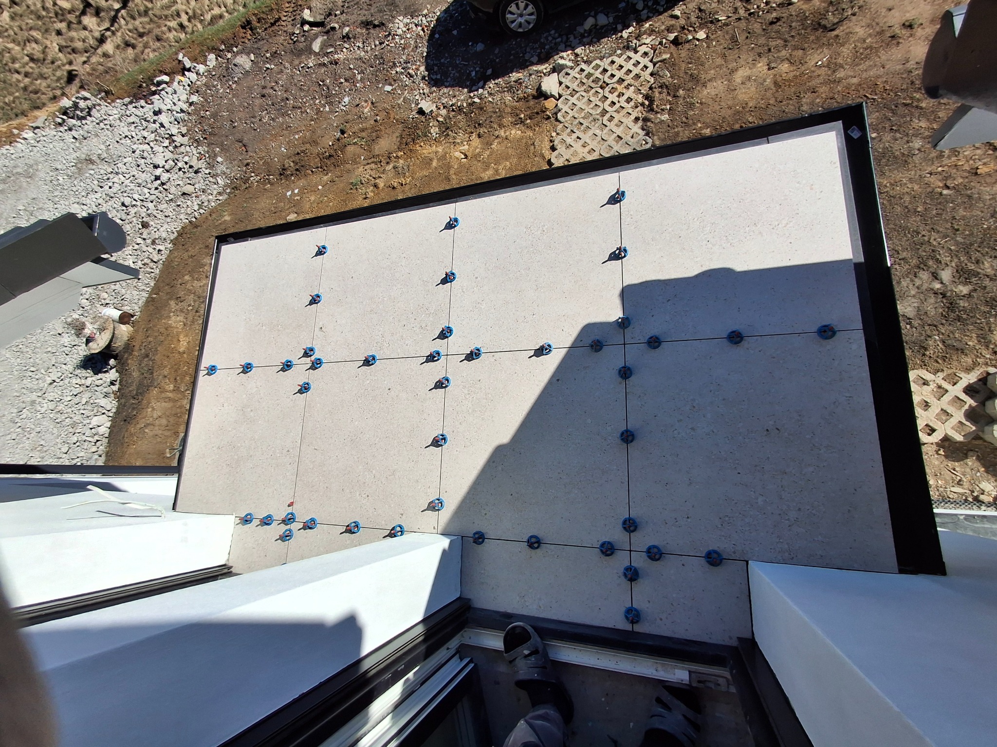 Montaż jasnych płyt na tarasie z użyciem systemu poziomowania, widok z góry na krawędź tarasu.