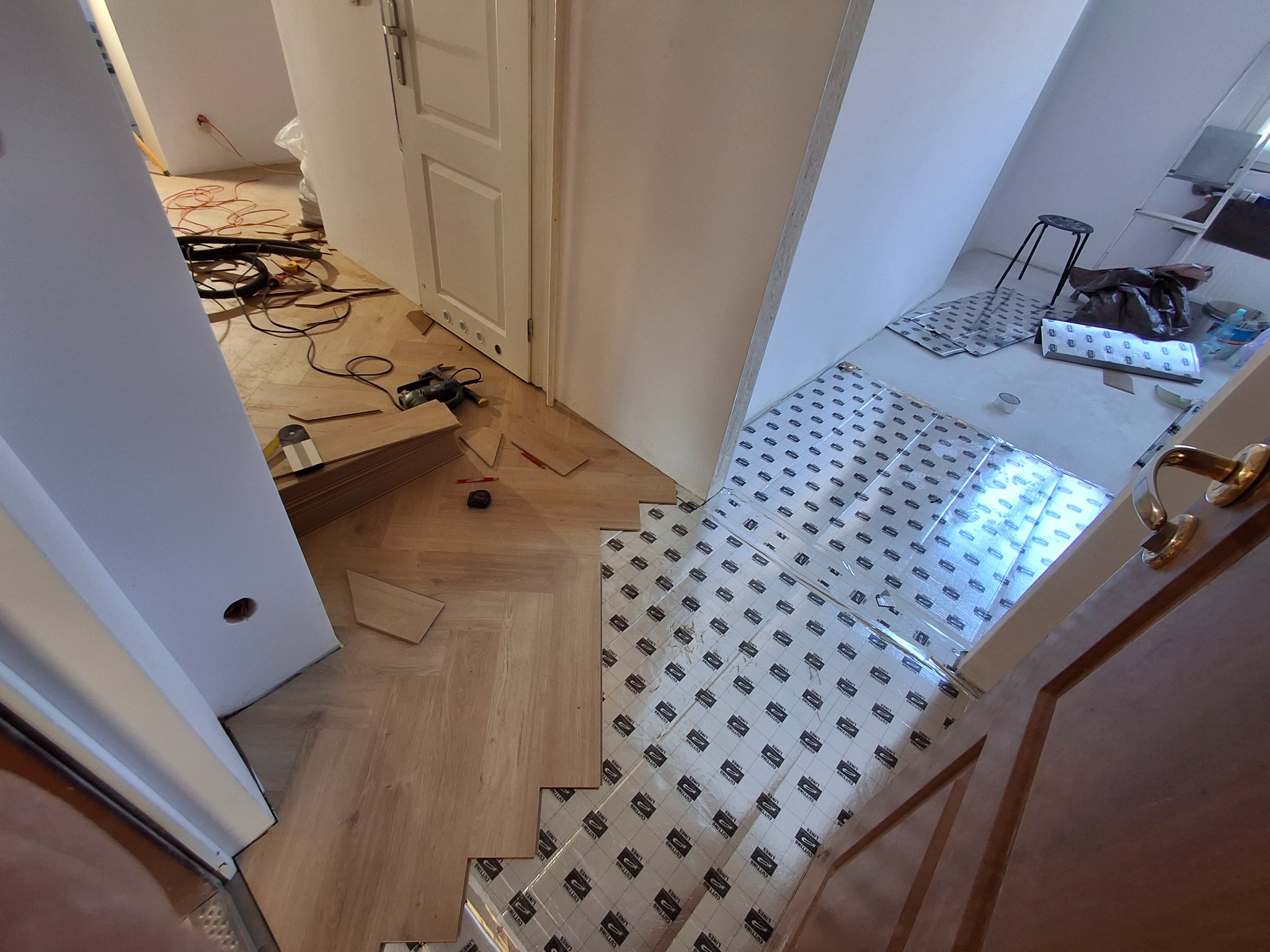 W trakcie układania paneli podłogowych w jodełkę w Łodygowicach: widoczny fragment ułożonej podłogi, podkład pod panele oraz narzędzia.