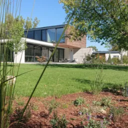 Nowoczesny dom z elementami drewna i dużymi przeszkleniami, widoczny z perspektywy ogrodu z ozdobnymi trawami i rabatami kwiatowymi.