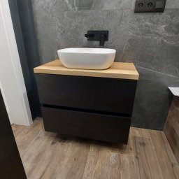 Meble na wymiar Bartosz Dopierała - Nowoczesna łazienka z umywalką nablatową na szafce z czarnymi frontami i drewnianym blatem, szara ściana z marmurowym wzorem, oświetlenie żarówką Edisona.