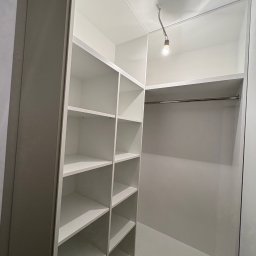 Meble na wymiar Bartosz Dopierała - Wnętrze szafy wnękowej z półkami po lewej i drążkiem na ubrania po prawej stronie. Białe wykończenie, oświetlenie punktowe u góry.