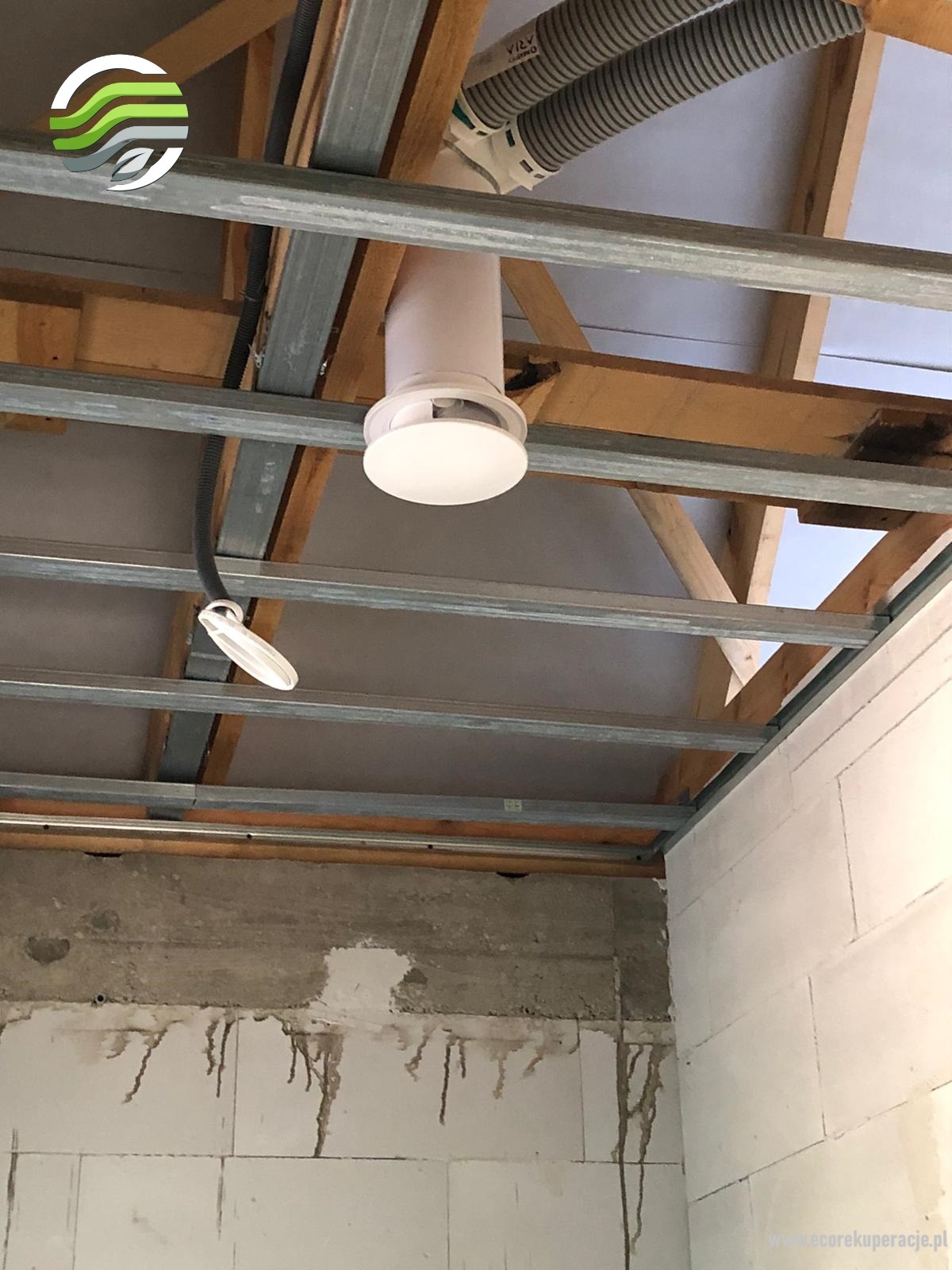 Biały, okrągły anemostat zamontowany w suficie podwieszanym, widoczne przewody wentylacyjne i konstrukcja sufitu.