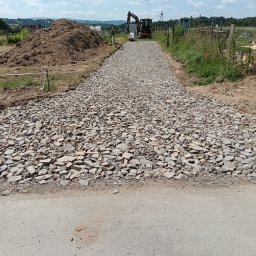 Kop-tech wladyslaw kawecki - Utwardzona droga z kamienia polnego, w tle koparka i pryzma ziemi. Widok z poziomu gruntu, słoneczny dzień.