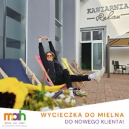 Uśmiechnięta kobieta w okularach przeciwsłonecznych relaksuje się na kolorowym leżaku przed kawiarnią 'Relax', z widocznym logo MAH i tekstem 'Wycieczka do Mielna do nowego klienta!'
