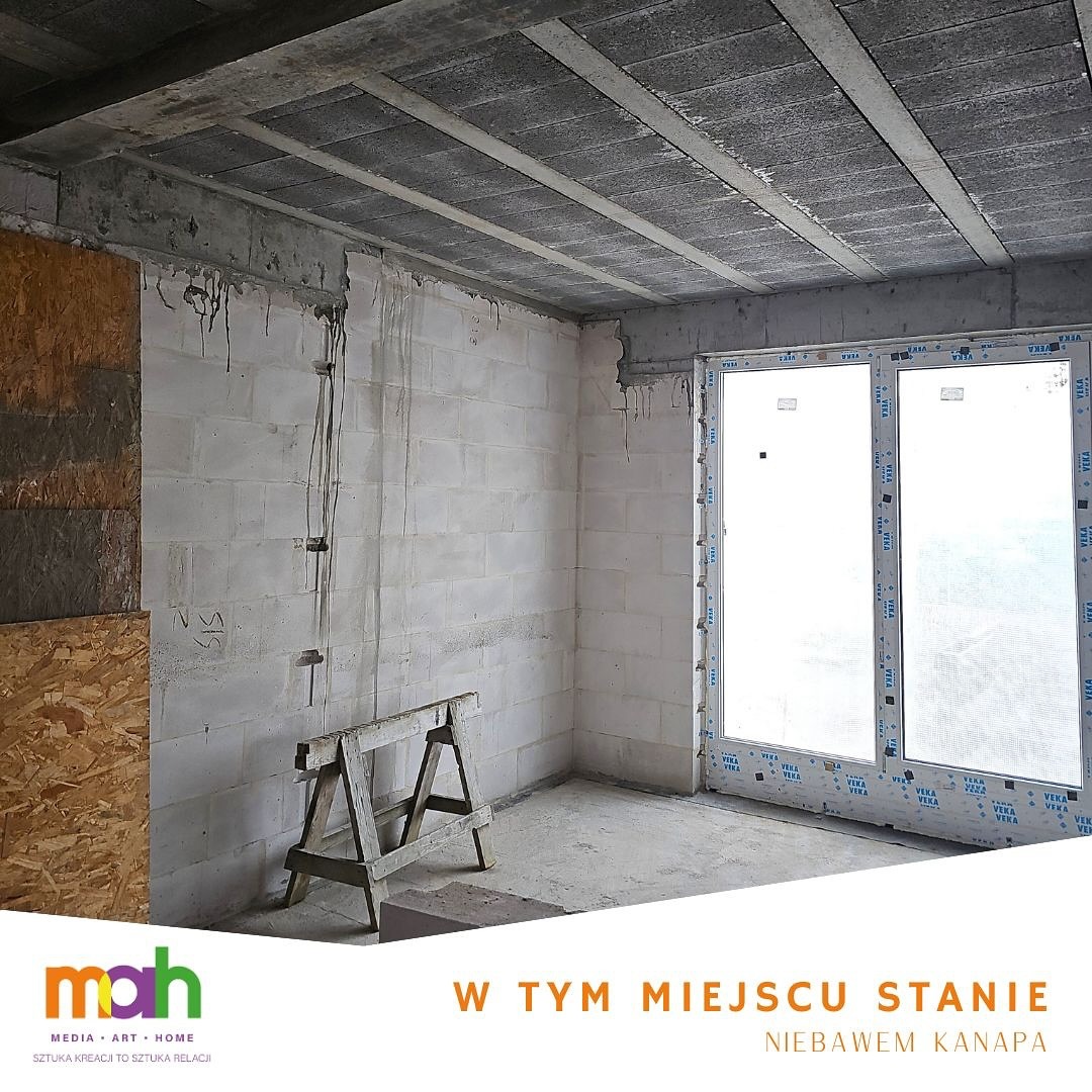 Surowe wnętrze w trakcie remontu: ściany z białych bloczków, surowy betonowy sufit z widocznymi belkami, duże okno PCV, drewniany kozioł na podłodze, instalacja elektryczna na ścianie.