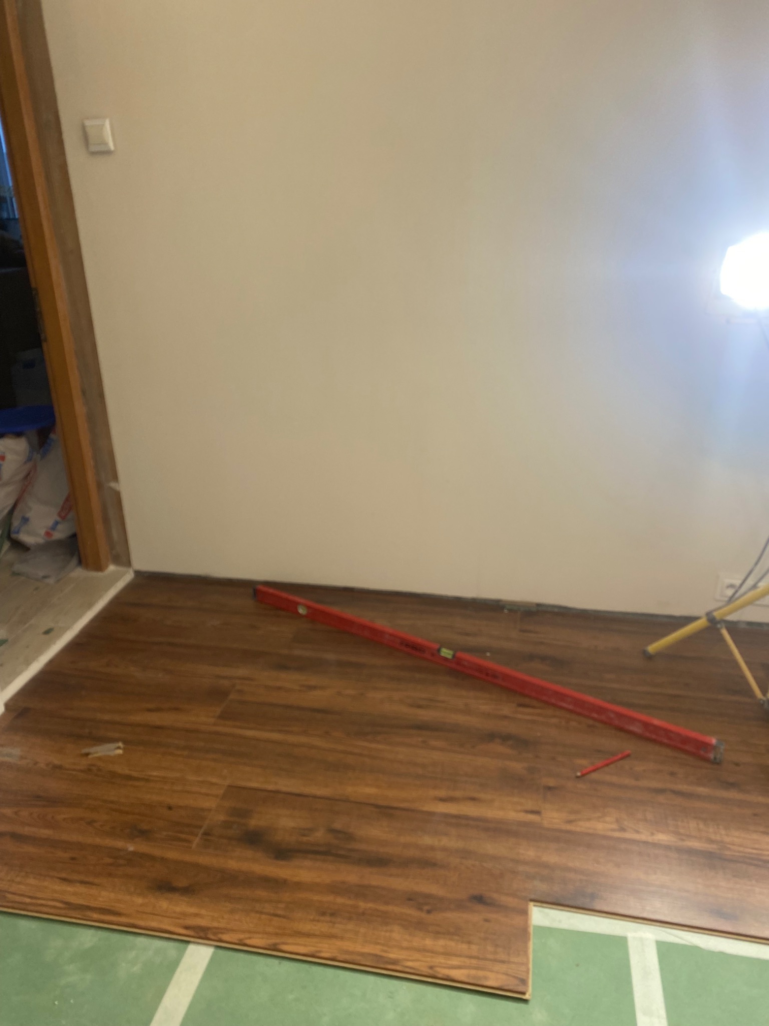 Układanie paneli podłogowych w trakcie pracy, widoczny poziomica, oświetlenie robocze i fragment podkładu. Ciepłe odcienie brązu paneli kontrastują z zielenią podkładu.