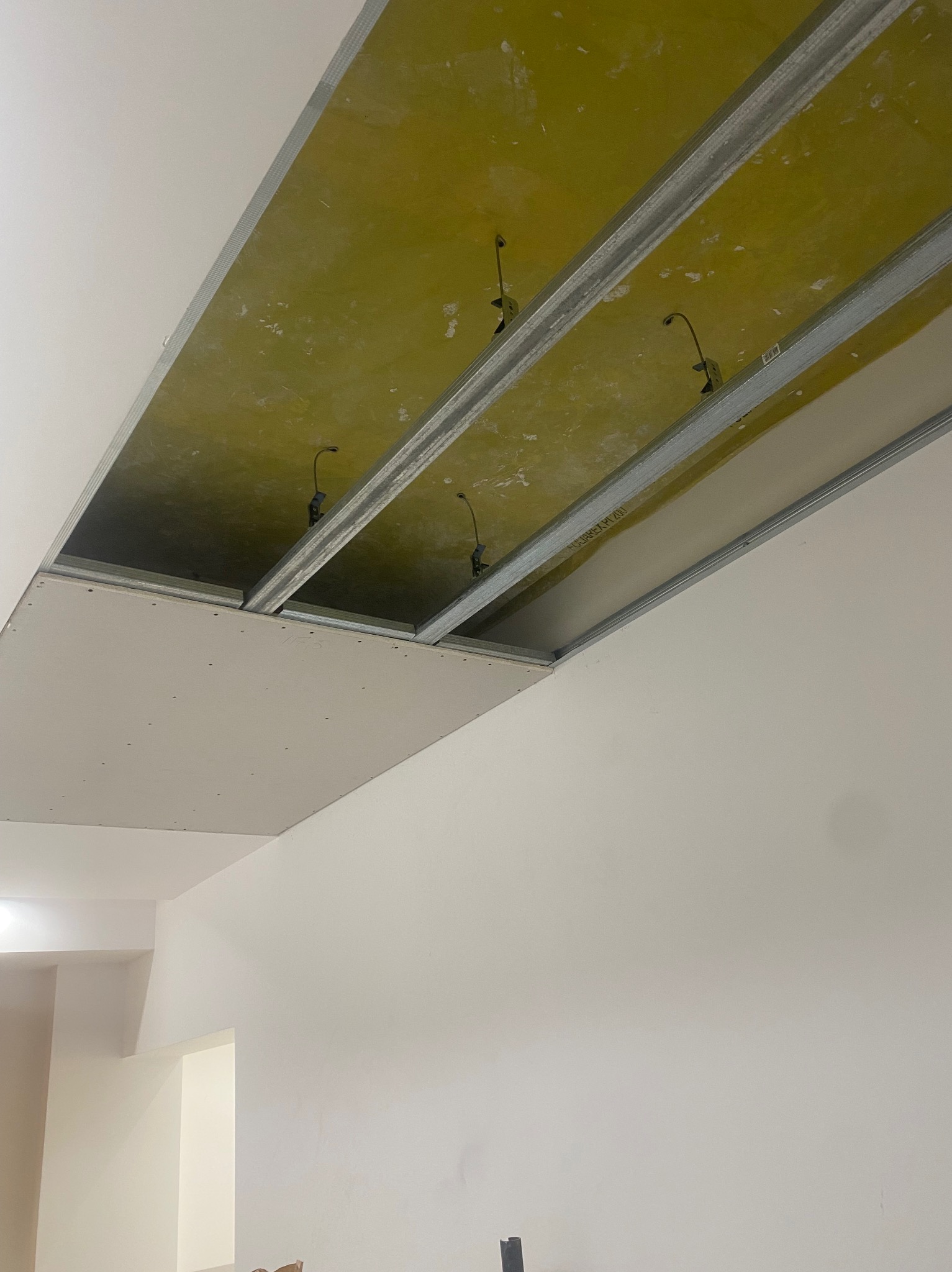 Montaż sufitu podwieszanego z płyt karton-gips na metalowej konstrukcji. Widoczne kable oświetleniowe. Świeżo zamontowana płyta. Białe ściany w tle.