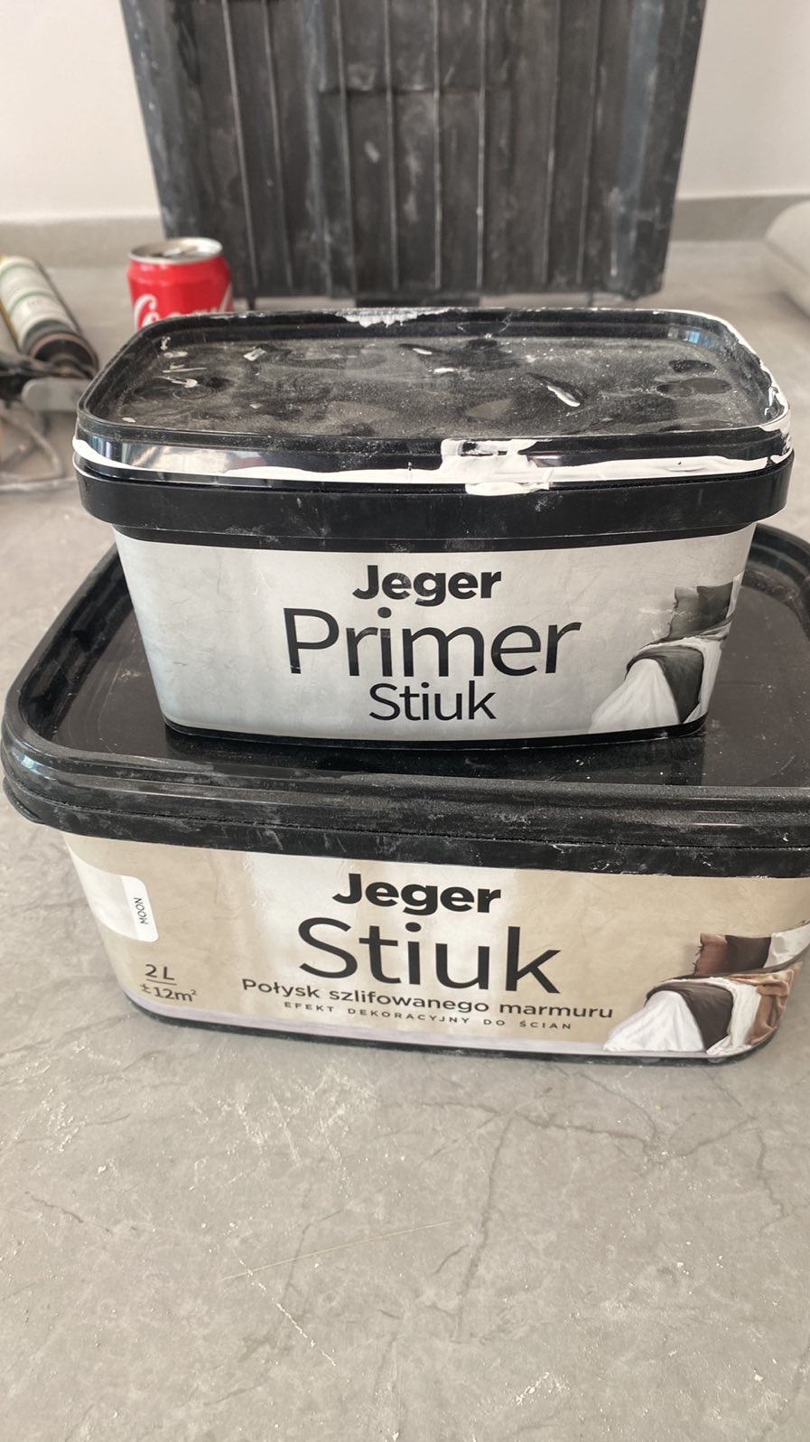 Dwa pojemniki z primerem i stiukiem Jeger, jeden na drugim, z widocznymi śladami użytkowania, sugerujące przygotowanie do prac wykończeniowych.