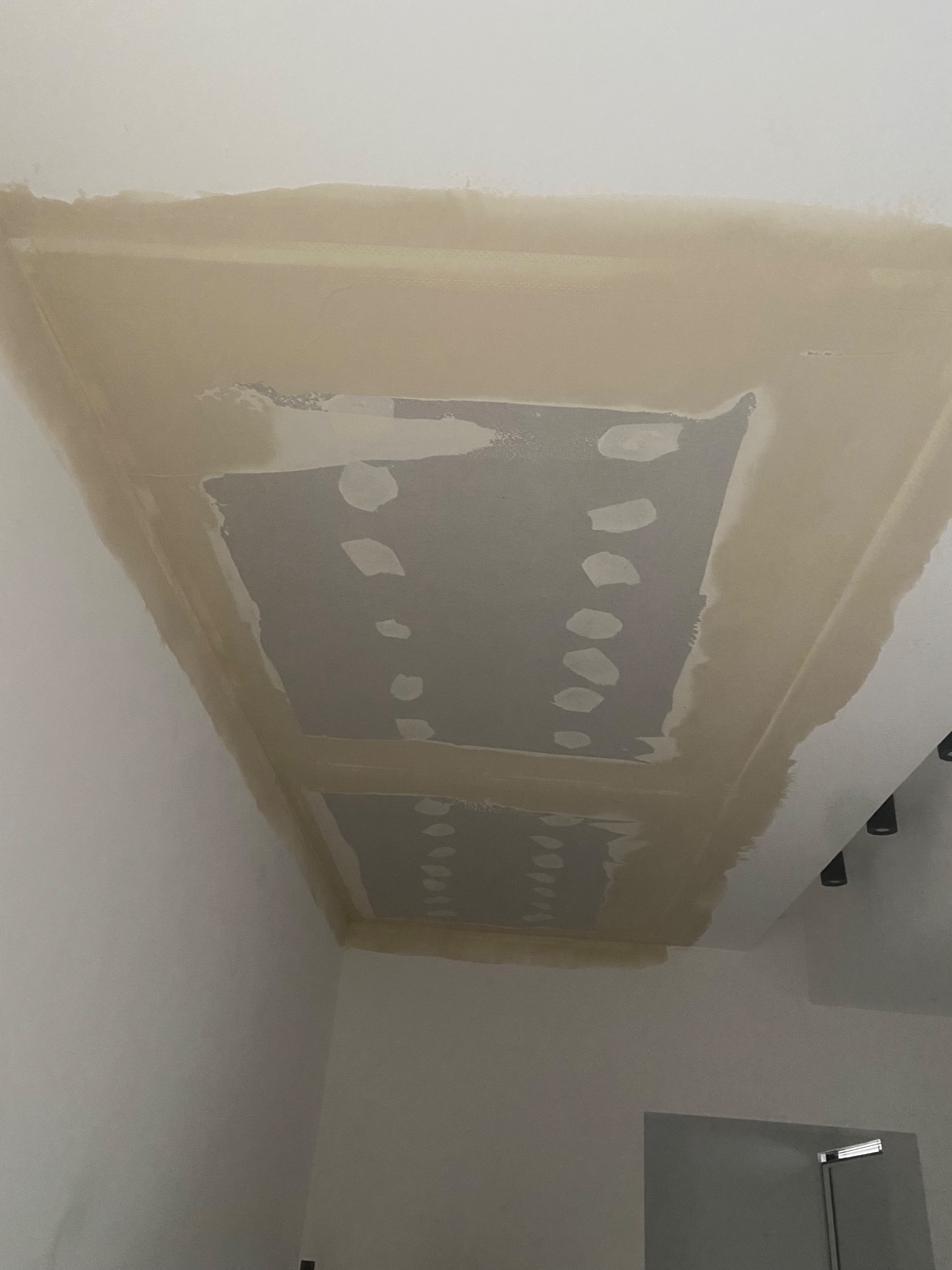 Sufit z wygładzoną wnęką, przygotowany do malowania. Widoczne ślady szpachlowania i gruntowania. Oświetlenie punktowe w tle. Ujęcie z dołu.