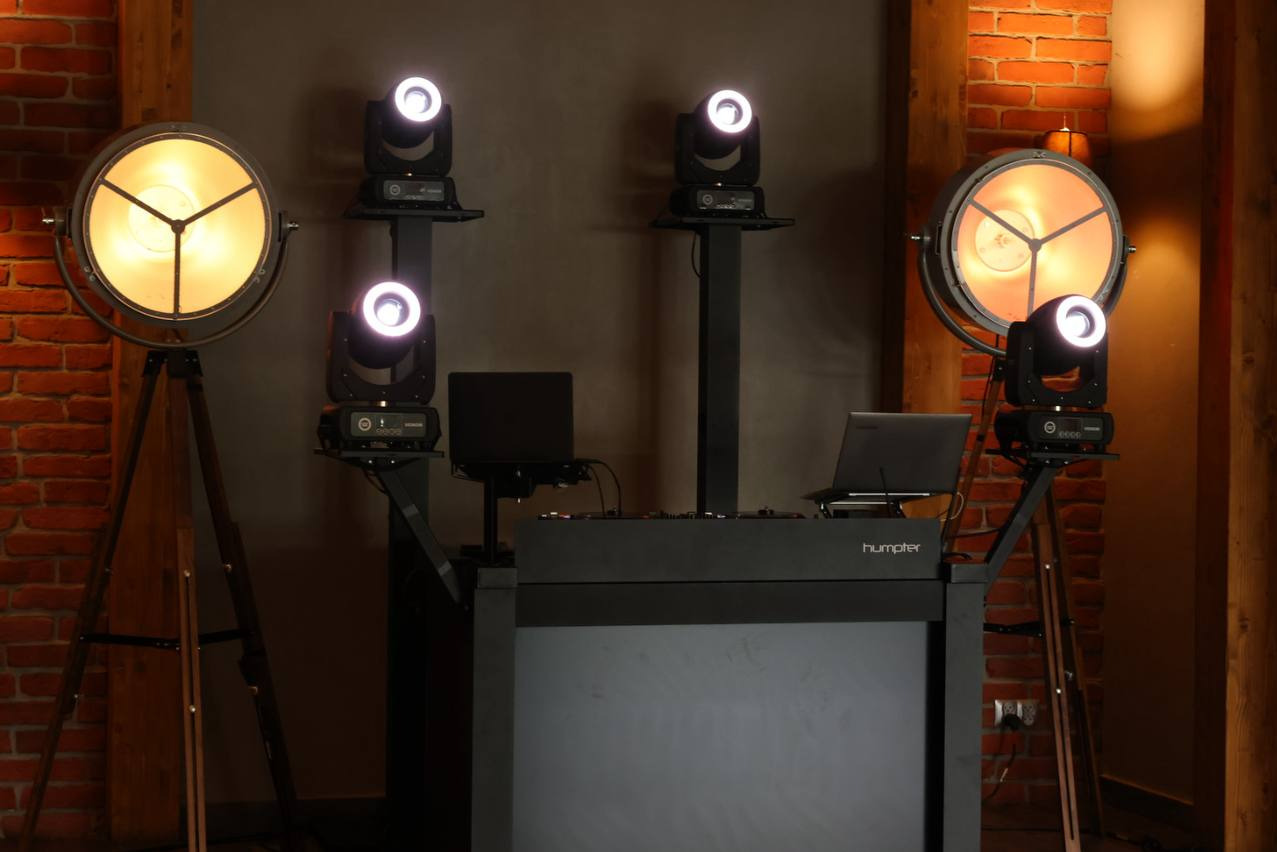 Profesjonalne nagłośnienie i oświetlenie eventowe z laptopami na tle ceglanej ściany i drewnianych elementów konstrukcyjnych.