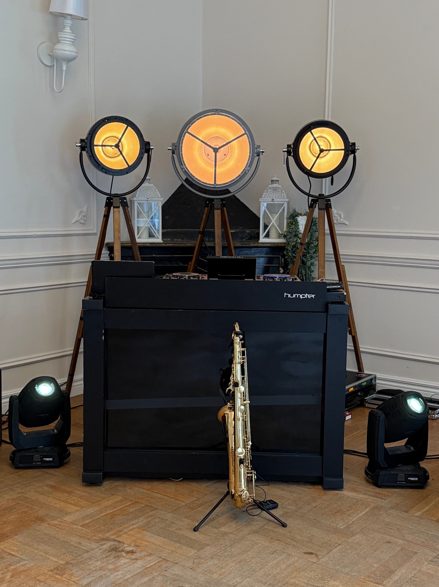 Scena z saksofonem na statywie, czarnym DJ-skim stanowiskiem Humper i trzema reflektorami na drewnianych trójnogach, oświetlającymi wnętrze w ciepłych barwach.