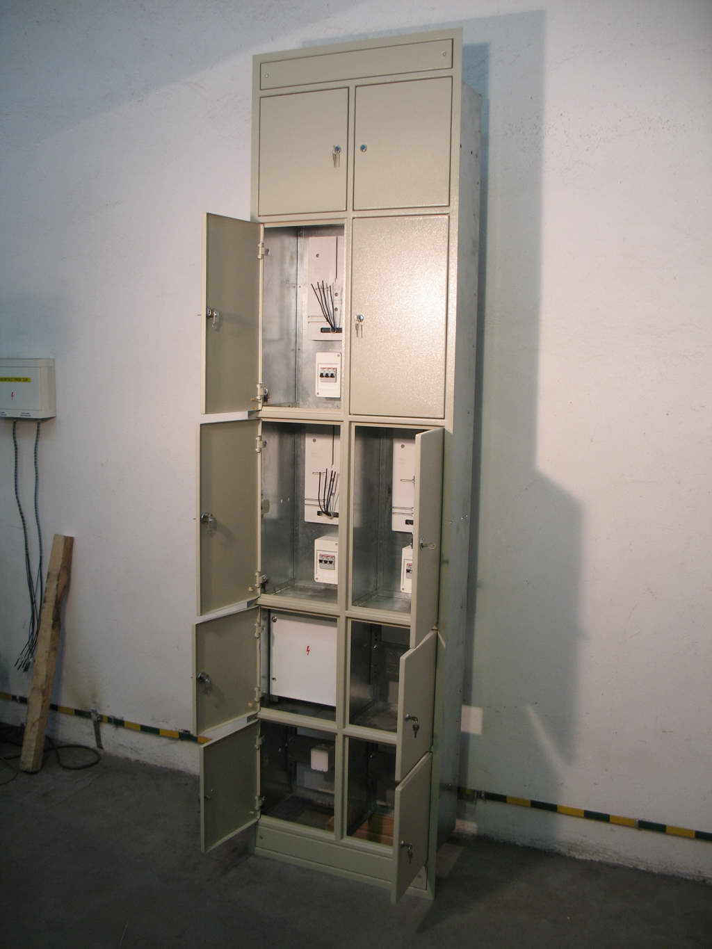 Wysoka, metalowa szafa rozdzielcza z kilkoma otwartymi drzwiczkami, ukazująca zainstalowane liczniki elektryczne i okablowanie wewnątrz, umieszczona w surowym pomieszczeniu z betonową podłogą...