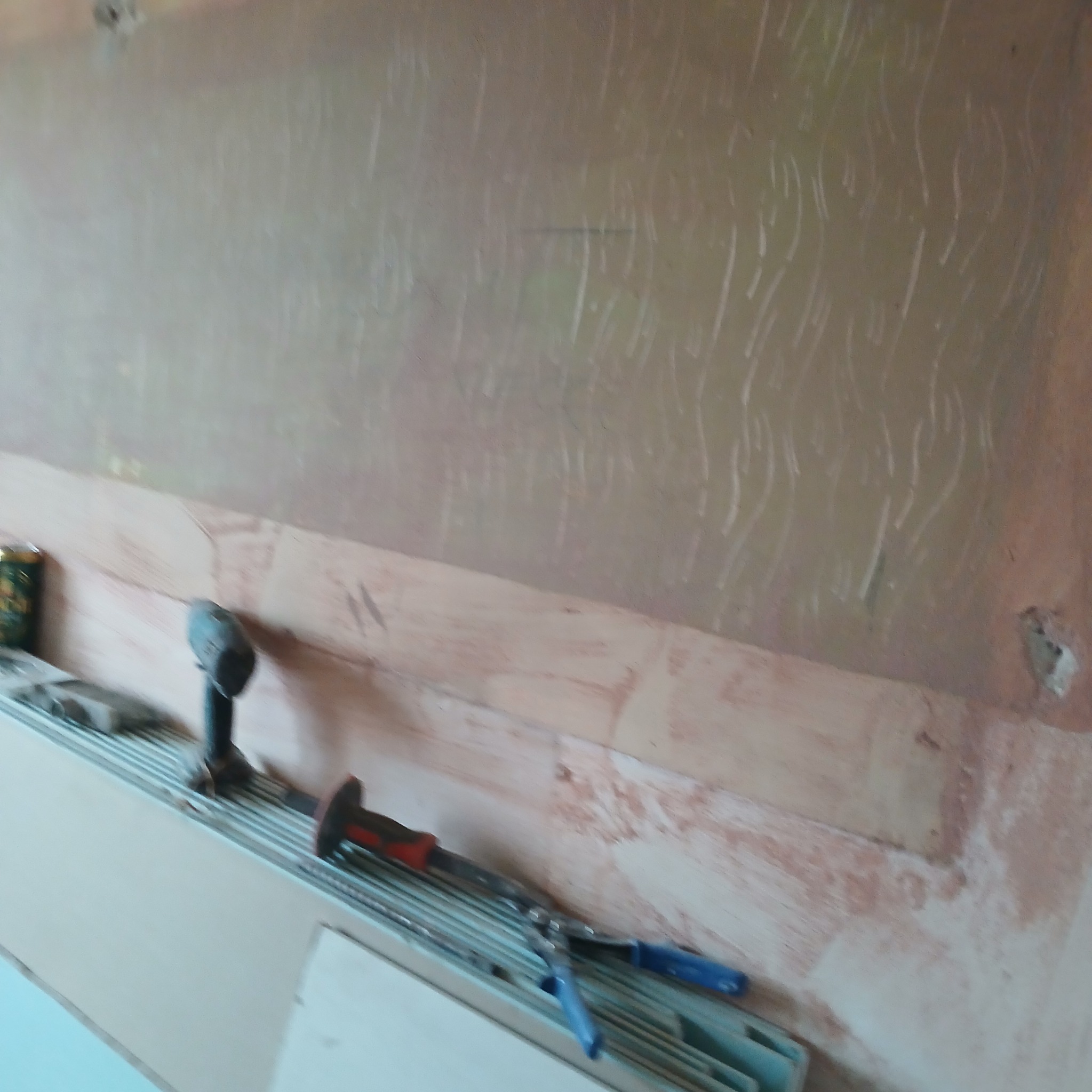 Ściana z nałożoną warstwą wstępną, widoczne narzędzia: wiertarka, młotek i szczypce do mocowania profili kartonowo-gipsowych, przygotowanie do montażu płyty gipsowej.