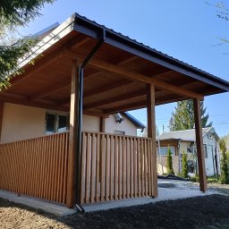 Usługi ogólnobudowlane - Drewniana altana z czarną rynną, osłonięta pionowymi listwami, przylegająca do budynku, z widocznym fragmentem ogrodu i niebem w tle.