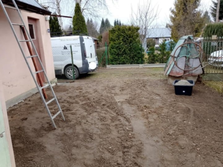 Teren przygotowany pod renowację elewacji budynku jednorodzinnego, widoczna drabina oparta o ścianę, zaparkowany samochód dostawczy z logo firmy oraz studnia z wiadrem wypełnionym piaskiem.